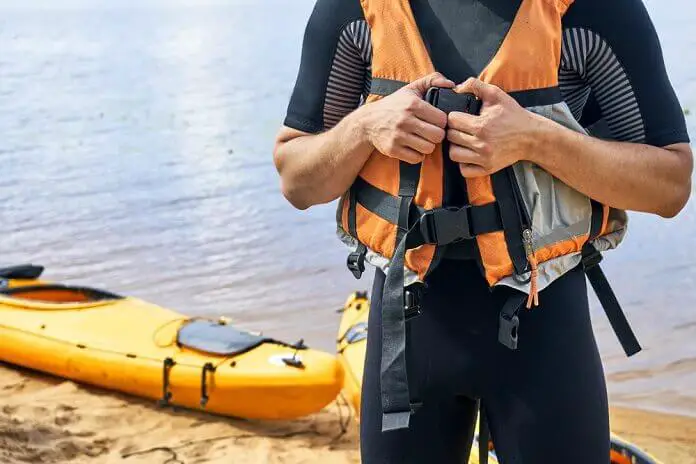 Young man wearing wetsuit putting on a life jacket before sailing