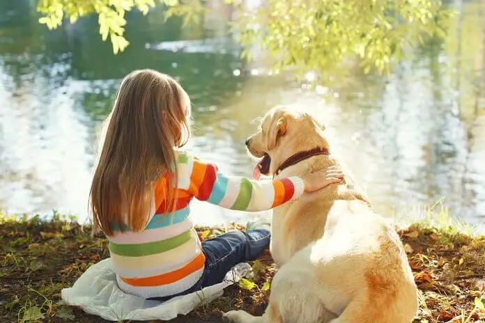 Two friends, child with Labrador retriever dog sitting in Jaycee Park near water 